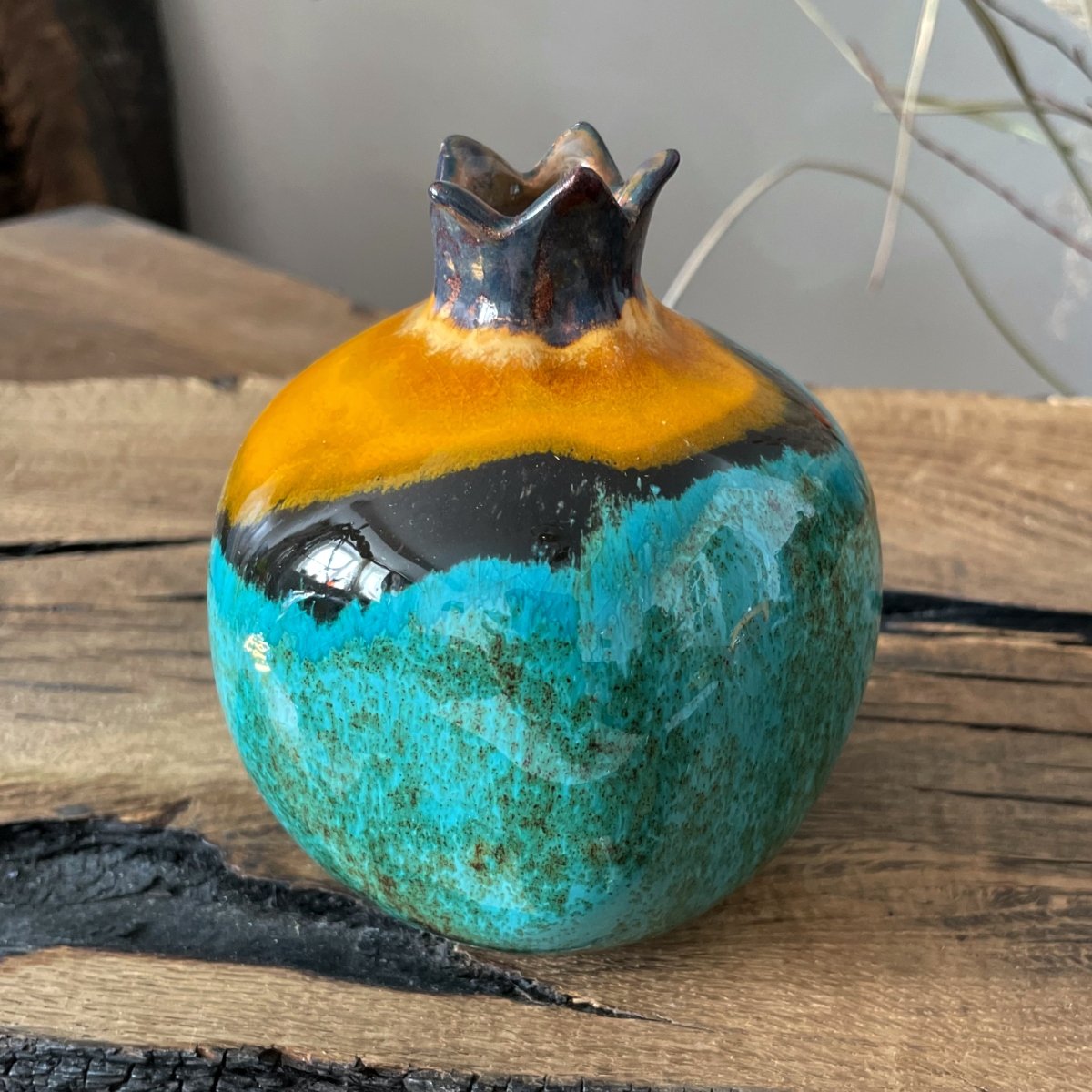 Decorative ceramic pomegranate on wooden table, turquoise glaze with bold yellow accent