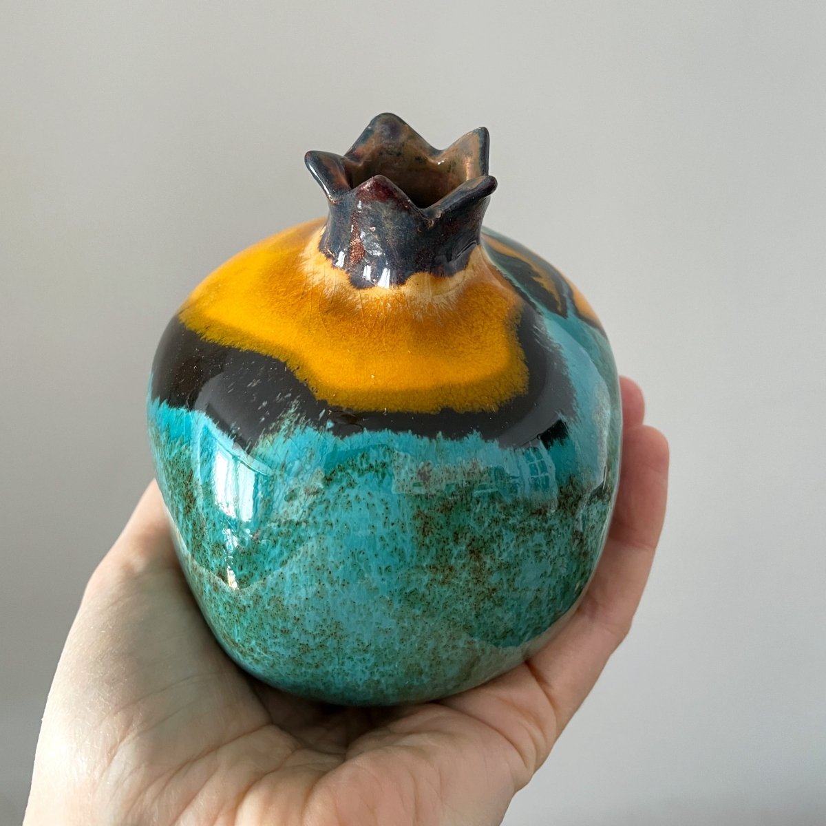 Handmade ceramic pomegranate with turquoise glaze and warm yellow accent, decorative pottery fruit in hand