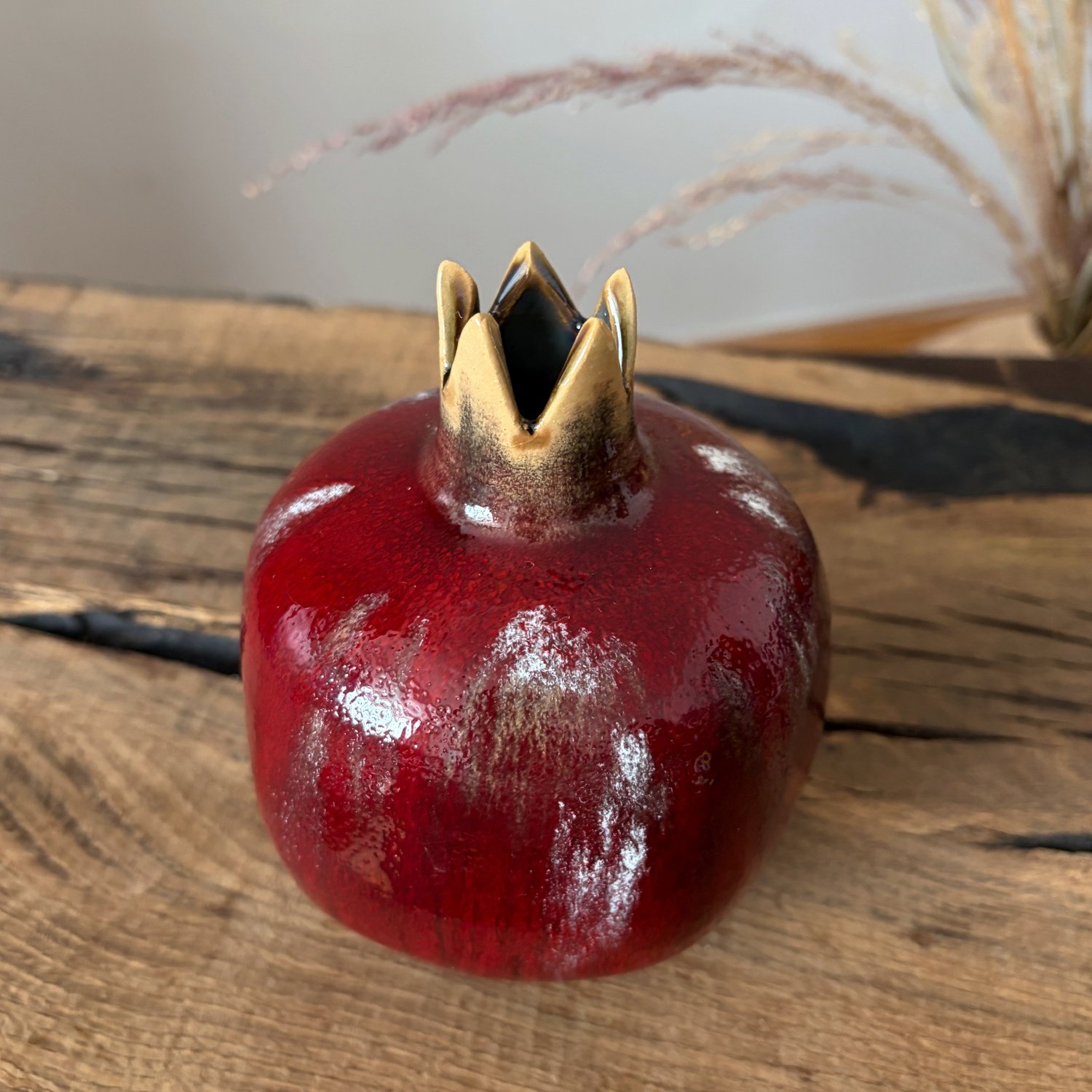 Red ceramic pomegranate vase displayed with dried flowers