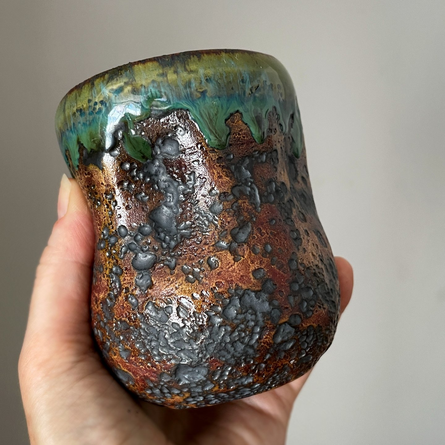 Handmade stoneware coffee cup held in hand for size reference